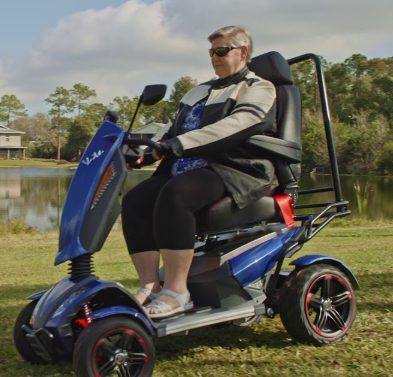 Person driving the EV Rider Vita Monster mobility scooter on a grassy field.