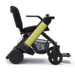 Black Whill Model F power wheelchair with a light green accent on the armrest, large wheels, and an under-seat storage basket.