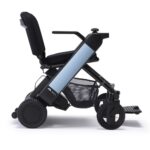 Whill Model F power wheelchair with light blue color armrests, featuring a modern design, large wheels, and a mesh storage basket.