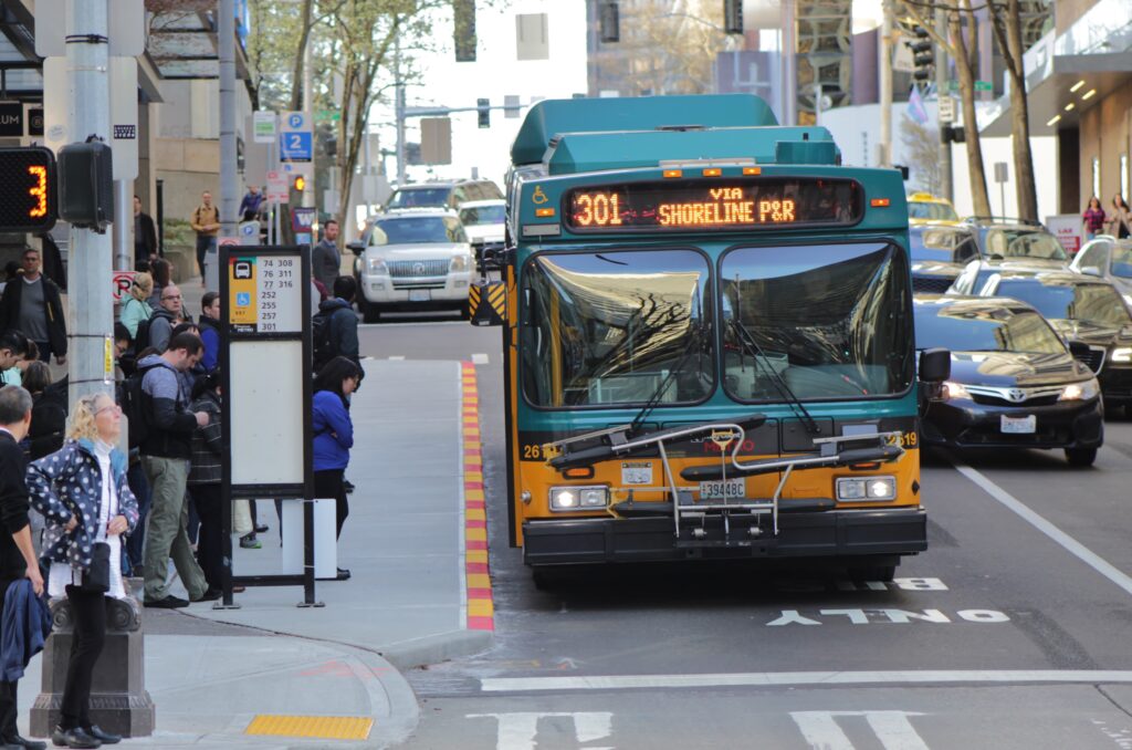 A King County Metro bus, route 301, stops on a busy downtown Seattle street with passengers waiting and traffic in the background.