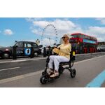 A stylish senior woman riding the eFOLDi Lite scooter on a city street, with the iconic London Eye in the background, symbolizing freedom and ease of mobility in busy urban environments.