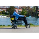Senior person looking content while riding the eFOLDi Explorer along a waterside path, highlighting the scooter's stable and comfortable design for leisurely outdoor activities.