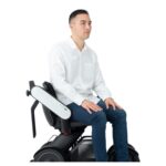 A young man sits comfortably in a Whill power chair, showing the ergonomic armrest and the chair's sleek design.