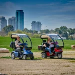 Live Style Image Side View of Blue Afiscooter S4 with Canopy Mobility Scooter, Red Afiscooter S3 Dual Seat Mobility Scooter with Canopy Golf Tires