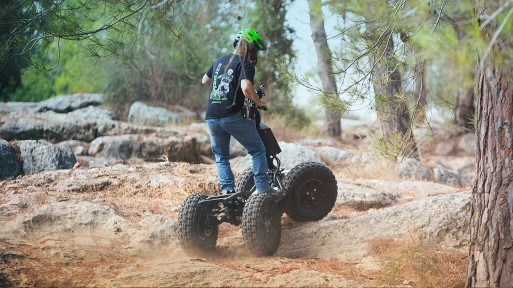 Rider wearing green helmet driving an EZRaider HD4 4x4 off-road electric scooter over rocky forest trail