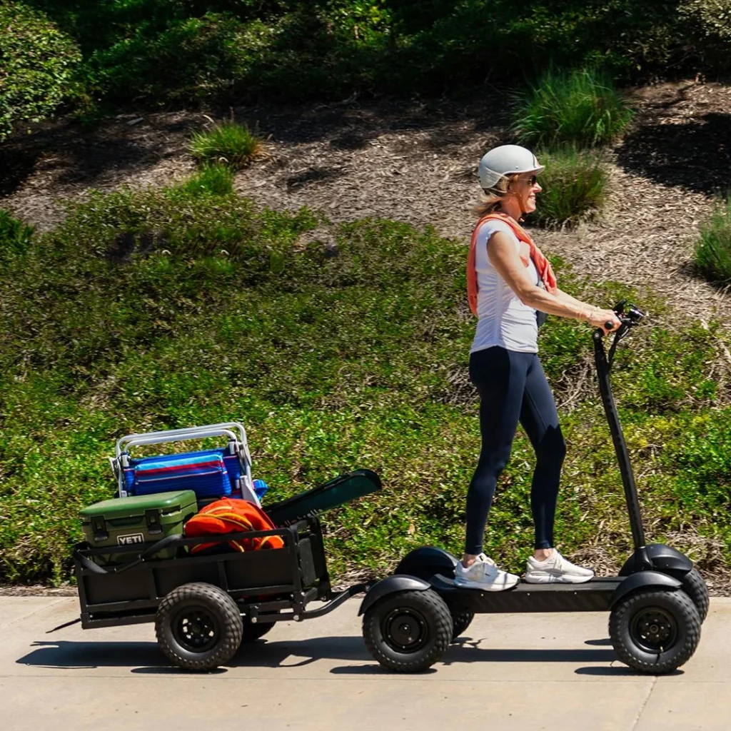 Woman riding CycleBoard X-Quad 3000 electric scooter towing a cargo trailer outdoors