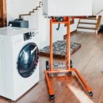 SuperHandy GUO097 material lift holding an appliance raised on its forks next to a washing machine